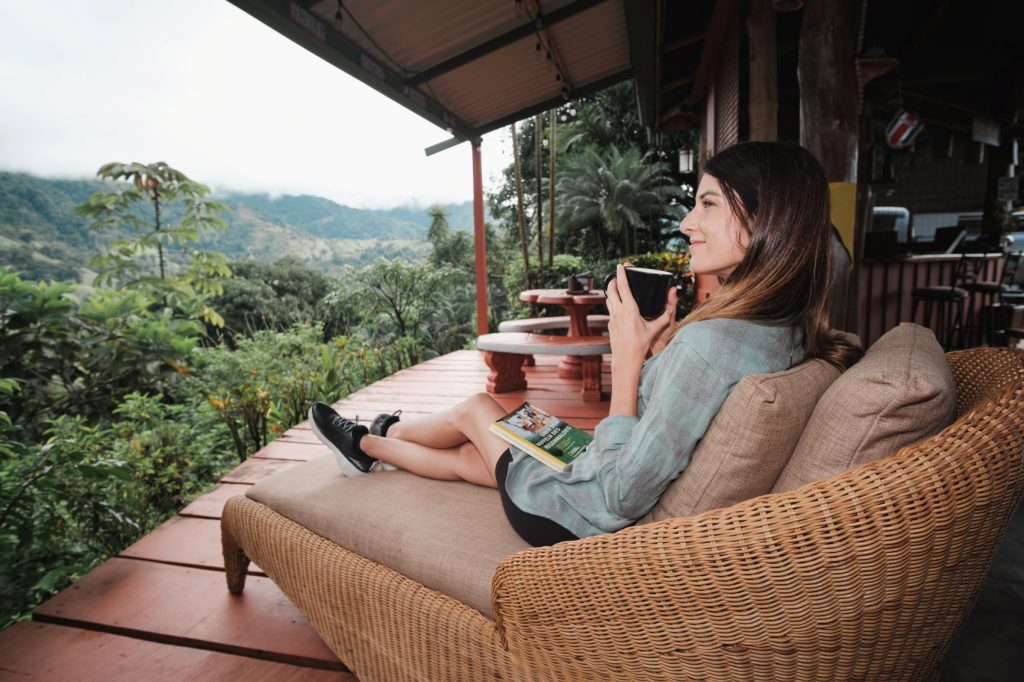 Santa Juana Quepos - Mujer adulta tomando café con un libro en un sillón con vista al bosque tropical gran angular