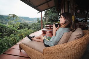 Santa Juana Quepos - Mujer adulta tomando café con un libro en un sillón con vista al bosque tropical gran angular