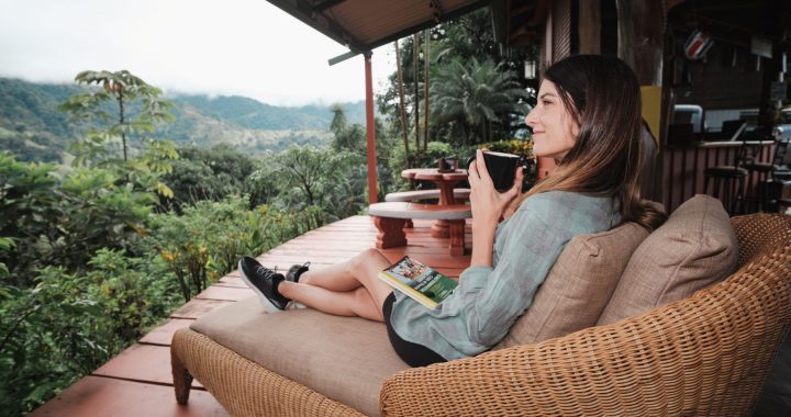 Santa Juana Quepos - Mujer adulta tomando café con un libro en un sillón con vista al bosque tropical gran angular
